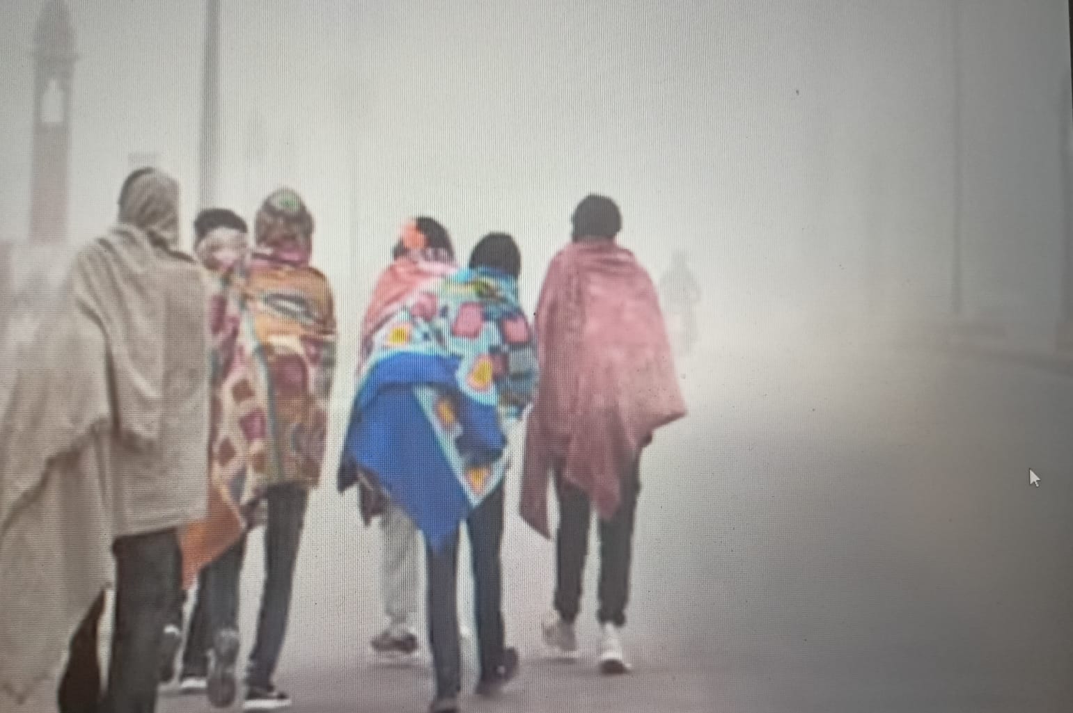 घने कोहरे के बीच सड़क पर लाइट जलाकर चलते वाहन और ठिठुरते लोग।