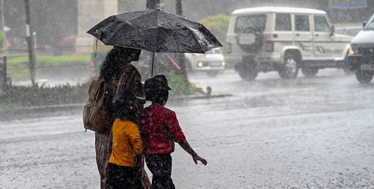 आसमान में उमड़ते-घुमड़ते काले मानसूनी बादलों और बारिश के बीच सड़क पर छाता लेकर चलते राहगीरों की एक सुंदर प्रतीकात्मक तस्वीर।