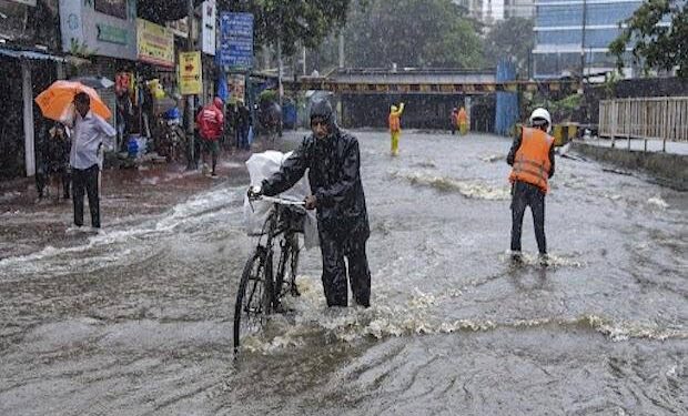 भारी मानसूनी बादलों से घिरा भोपाल का बड़ा तालाब और सड़क पर मूसलाधार बारिश के बीच छाता लेकर चलते राहगीरों की प्रतीकात्मक तस्वीर।